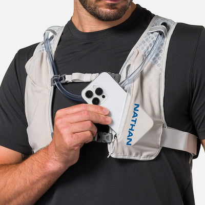 color:Vapor Grey/Deep Blue||seo:Nathan QuickStart 3.0 4 Liter Hydration Pack - Vapor Grey/Deep Blue - On Model - Model Pulling iPhone From Front Zippered Pocket
