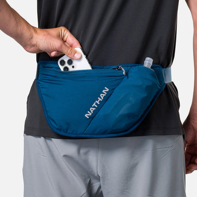 color:Sailor Blue/Reflective Silver||seo:Nathan Pinnacle FeatherLite Unisex Hydration Waist Belt - Sailor Blue/Reflective Silver - Model Pulling iPhone from Zippered Pocket