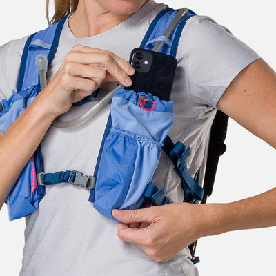 color:Periwinkle/Estate Blue||seo:Nathan TrailMix 2.0 12 Liter Unisex Hydration Pack - Periwinkle/Estate Blue - Female Runner Pulling iPhone From Front Storage Pocket