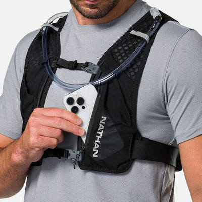 color:Black/Reflective Silver||seo:Nathan QuickStart 3.0 6 Liter Hydration Pack - Black/Reflective Silver - On Model - Model Pulling iPhone From Front Zippered Pocket