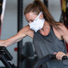White Play Safe Face Mask Lifestyle Image – Female Model Wearing Protective Safety Face Mask in the Gym while on an Elliptical - Left Angle