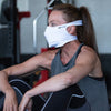 White Play Safe Face Mask Lifestyle Image – Female Model Wearing Protective Safety Face Mask in the Gym while Sitting Down - Left Angle